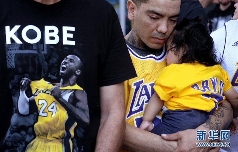 在美國洛杉磯斯台普斯中心外，一名球迷抱著女兒觀看追思會現場直播。新華社/美聯